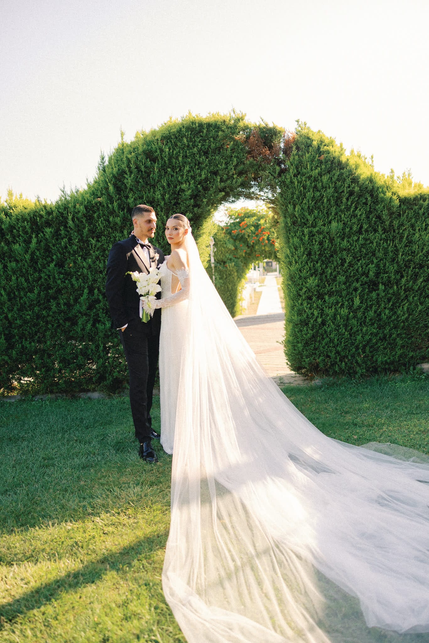 Şekilli çit kemerinin altında duran gelin ve damat