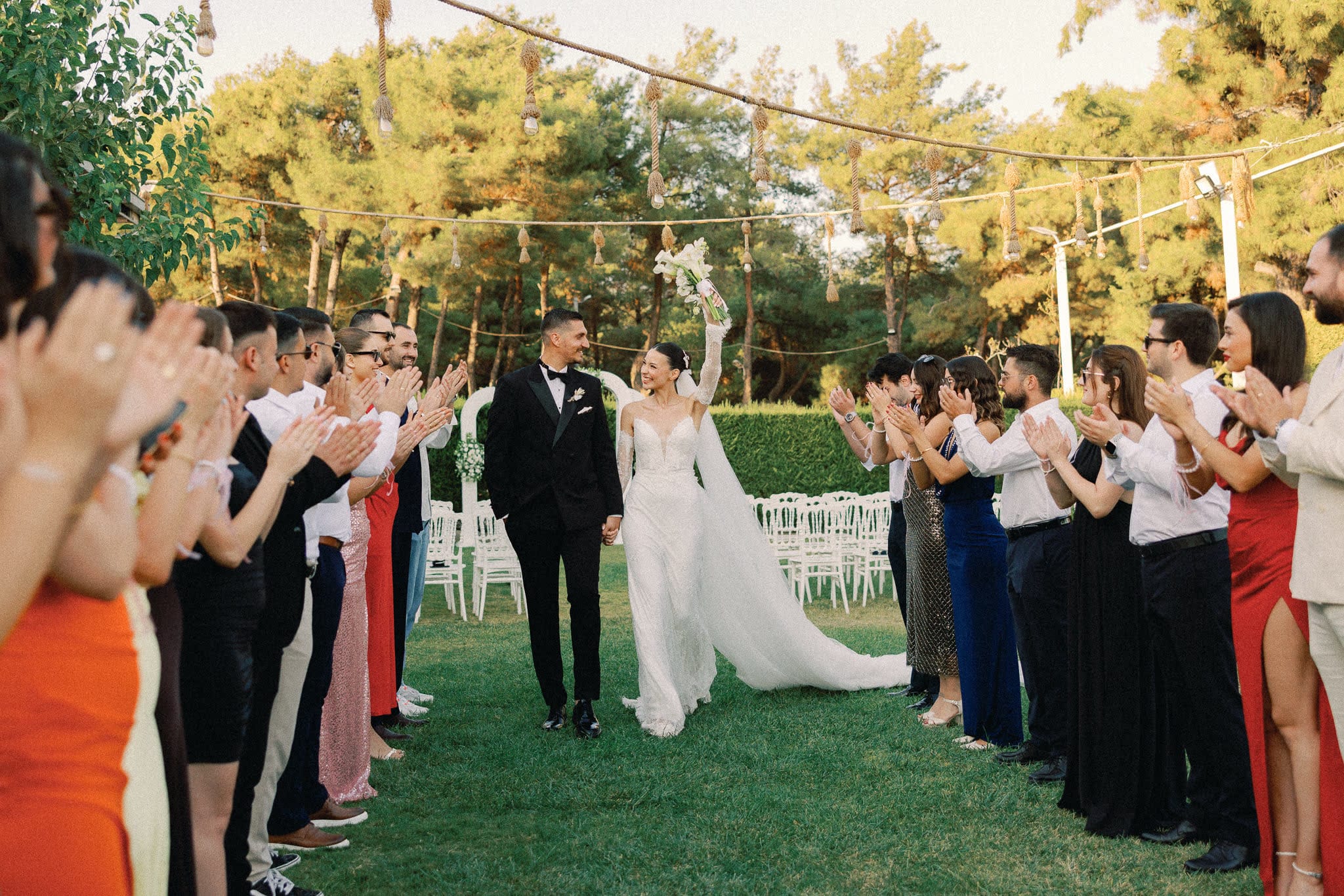 Gün batımında ip fenerlerin altında, alkışlayan davetlilerin arasından yürüyen gelin ve damat