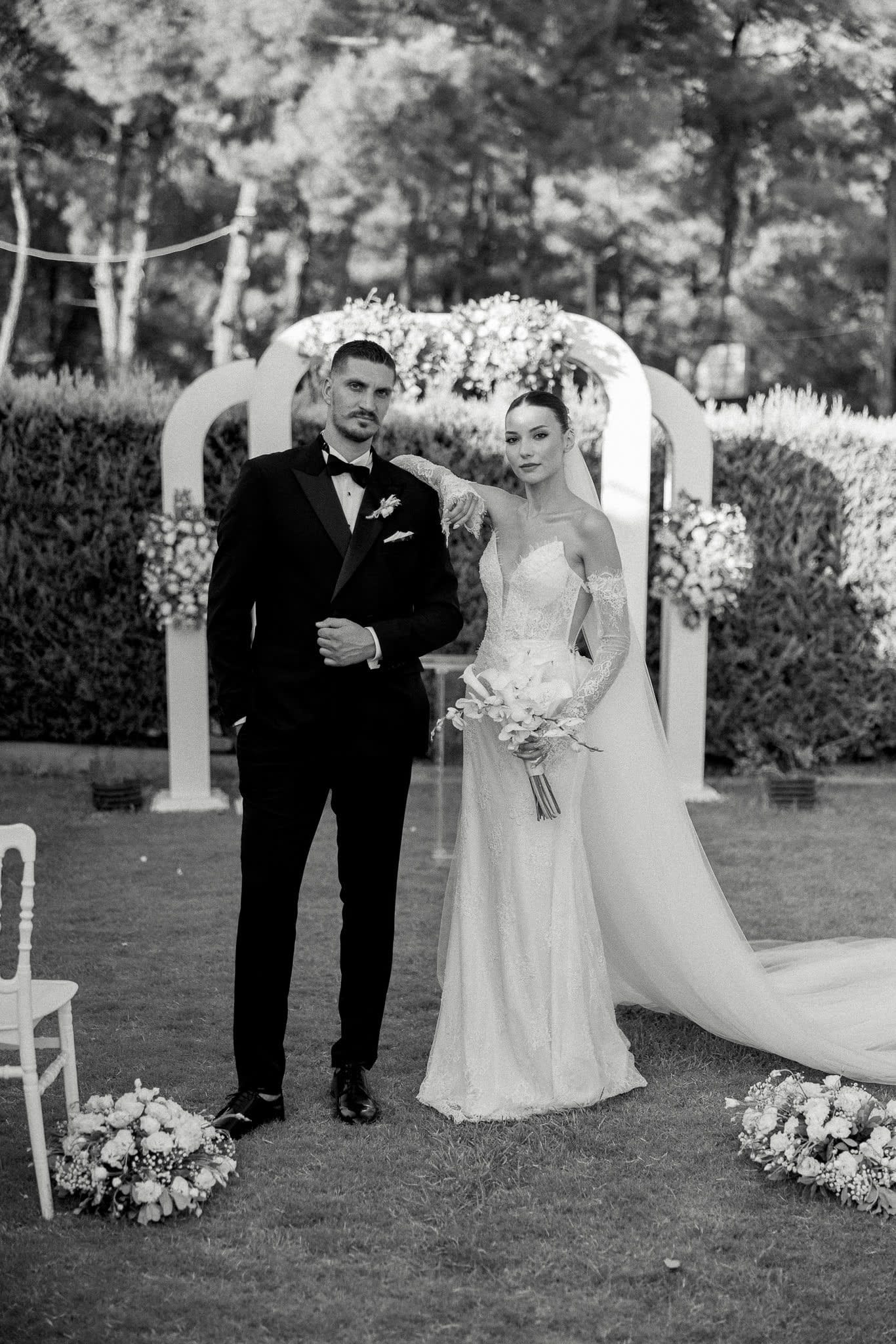 Tören kemerinin önünde duran gelin ve damat — siyah-beyaz kare